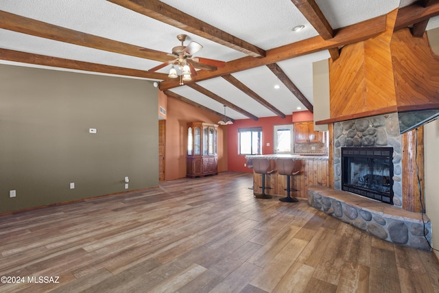 unfurnished living room featuring hardwood / wood-style flooring, lofted ceiling with beams, a textured ceiling, ceiling fan, and a stone fireplace