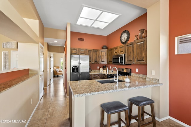 kitchen with sink, appliances with stainless steel finishes, a kitchen breakfast bar, light stone countertops, and kitchen peninsula