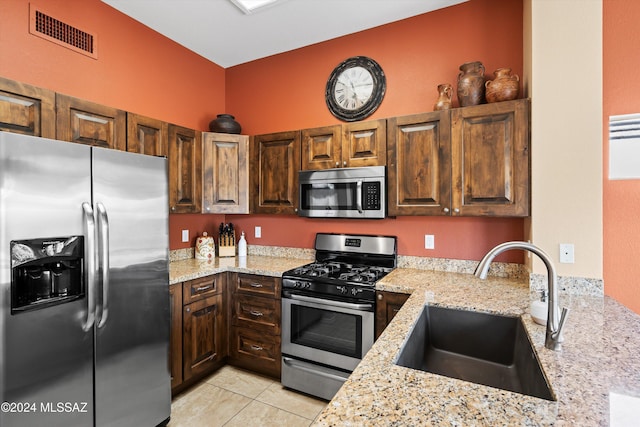 kitchen featuring stainless steel appliances, light stone countertops, sink, and light tile patterned floors