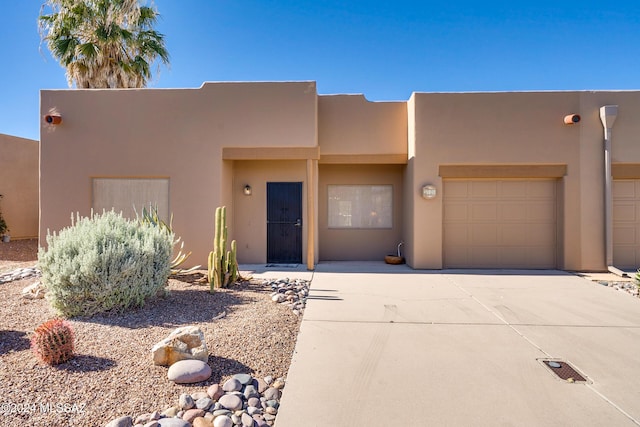 pueblo-style home with driveway, a garage, and stucco siding