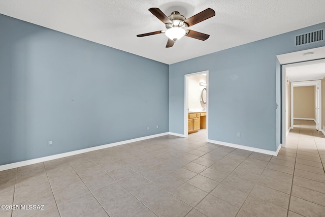 spare room featuring a textured ceiling, light tile patterned floors, visible vents, baseboards, and a ceiling fan