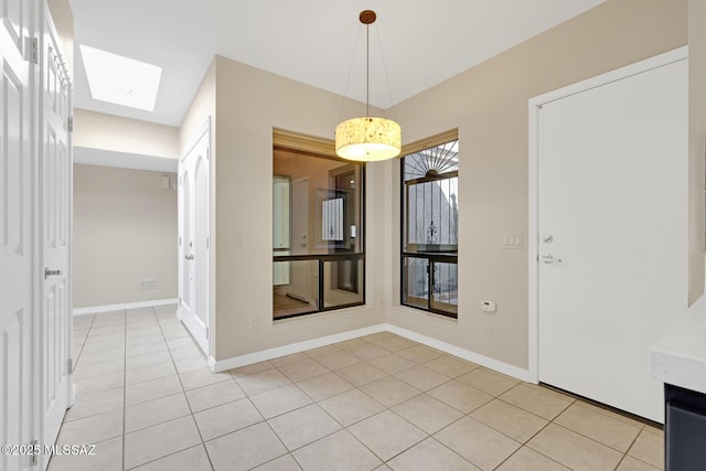 unfurnished dining area with a skylight, light tile patterned floors, and baseboards