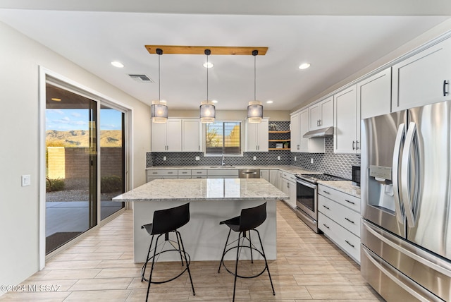 kitchen with a center island, light stone countertops, hanging light fixtures, and appliances with stainless steel finishes