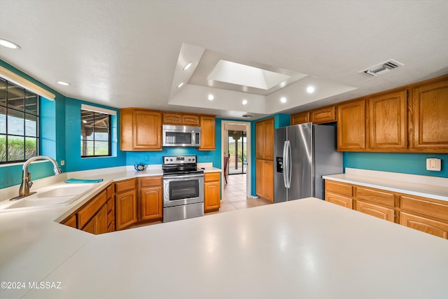 kitchen with sink, a textured ceiling, appliances with stainless steel finishes, a tray ceiling, and light tile patterned flooring