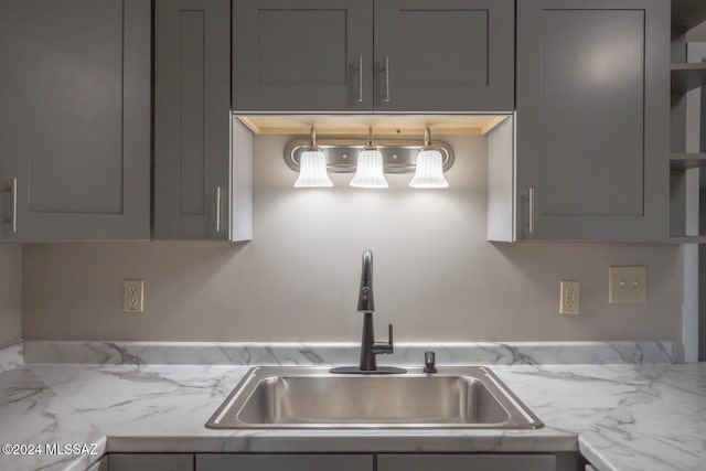 kitchen with gray cabinetry, light stone countertops, and sink