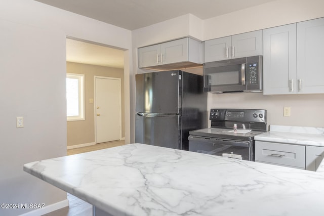 kitchen with gray cabinetry, black electric range oven, refrigerator, light stone countertops, and light hardwood / wood-style floors