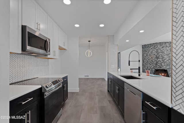 kitchen with a tiled fireplace, white cabinets, hanging light fixtures, sink, and appliances with stainless steel finishes