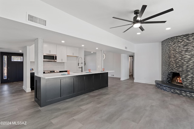 kitchen with a stone fireplace, sink, white cabinetry, and a large island