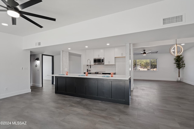 kitchen with white cabinetry, backsplash, sink, ceiling fan, and a spacious island