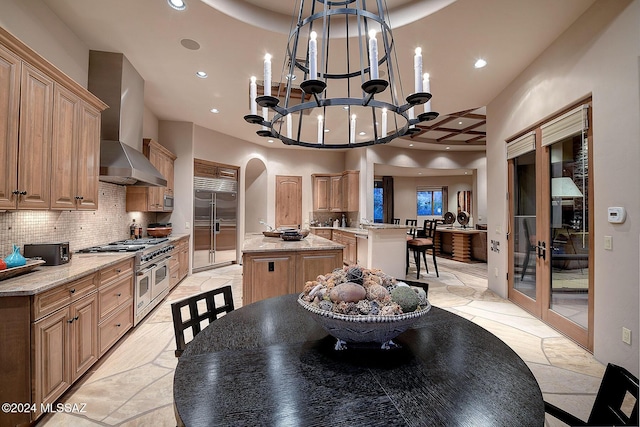 kitchen featuring a center island, wall chimney exhaust hood, a notable chandelier, backsplash, and high quality appliances