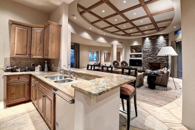 kitchen featuring sink, coffered ceiling, light stone counters, kitchen peninsula, and a breakfast bar