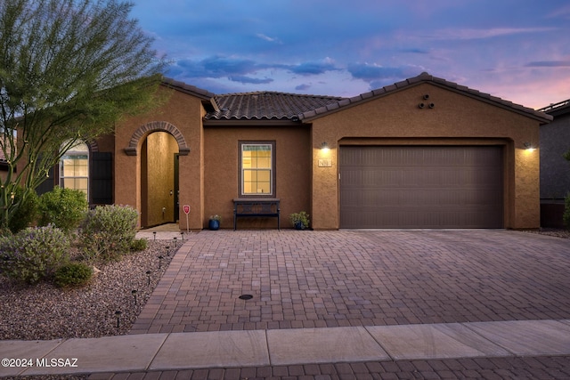 mediterranean / spanish-style home with an attached garage, a tile roof, decorative driveway, and stucco siding