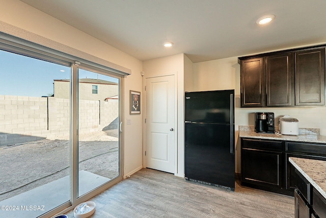 kitchen with dark brown cabinets, light hardwood / wood-style floors, black fridge, and light stone counters