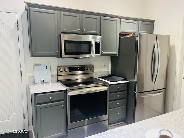 kitchen featuring gray cabinetry, appliances with stainless steel finishes, and light stone counters