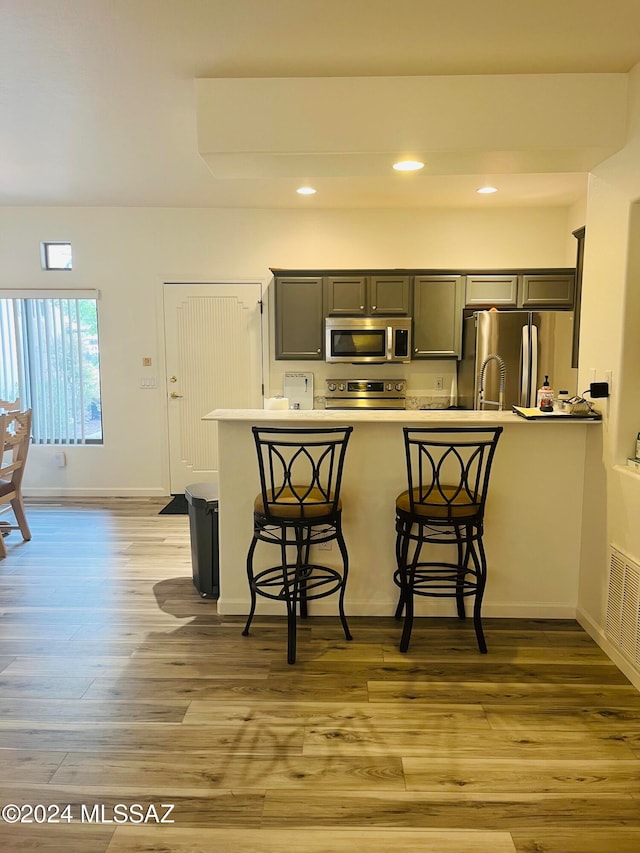 kitchen featuring a kitchen bar, kitchen peninsula, appliances with stainless steel finishes, and light hardwood / wood-style flooring