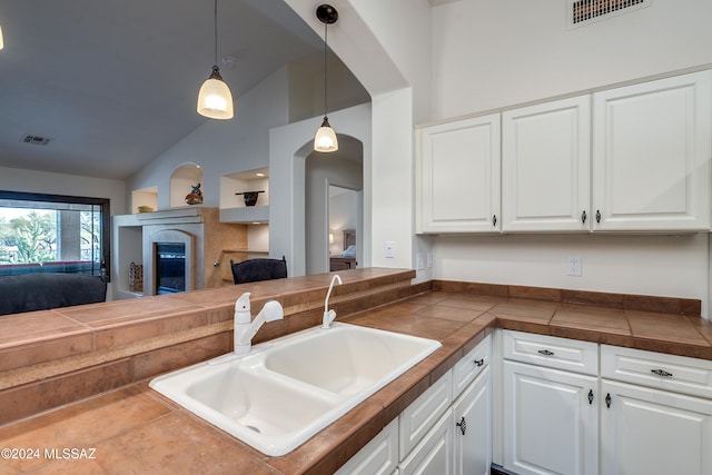 kitchen featuring vaulted ceiling, decorative light fixtures, white cabinetry, sink, and kitchen peninsula