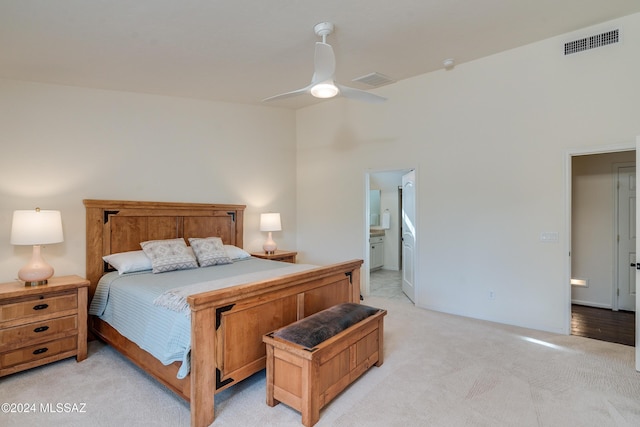 bedroom with ensuite bathroom, light carpet, and ceiling fan