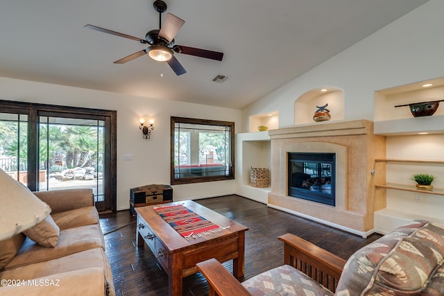 living room with vaulted ceiling, built in features, ceiling fan, a premium fireplace, and dark wood-type flooring