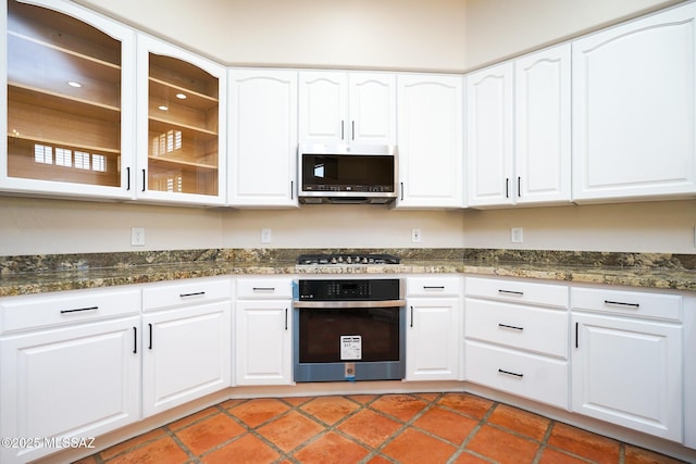 kitchen featuring white cabinetry, glass insert cabinets, stainless steel appliances, and dark stone counters