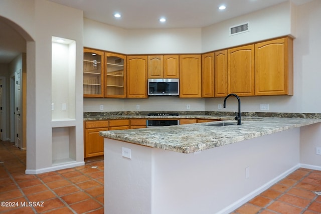 kitchen with light stone countertops, appliances with stainless steel finishes, kitchen peninsula, sink, and light tile patterned flooring