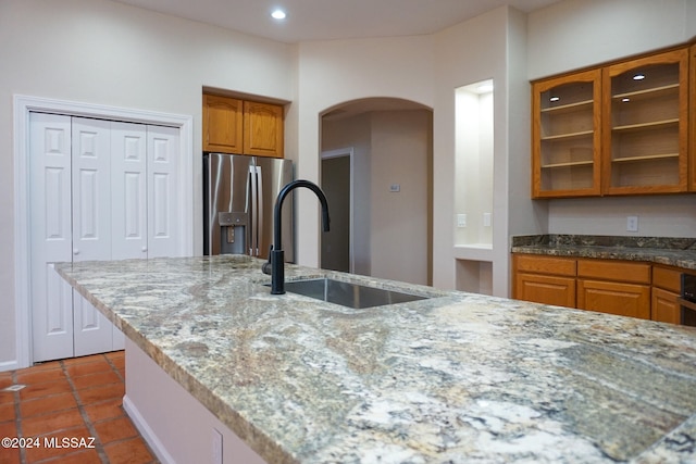 kitchen with stainless steel fridge, light stone counters, tile patterned floors, and sink