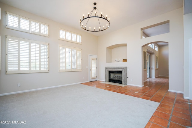 unfurnished living room featuring a healthy amount of sunlight, a towering ceiling, a notable chandelier, and a high end fireplace