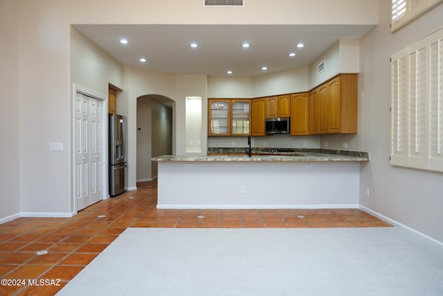 kitchen featuring tile patterned floors, kitchen peninsula, light stone countertops, and appliances with stainless steel finishes