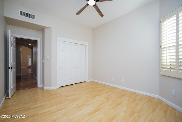 unfurnished bedroom featuring baseboards, visible vents, arched walkways, and wood finished floors