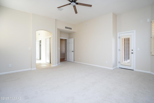 unfurnished room with arched walkways, light colored carpet, visible vents, ceiling fan, and baseboards