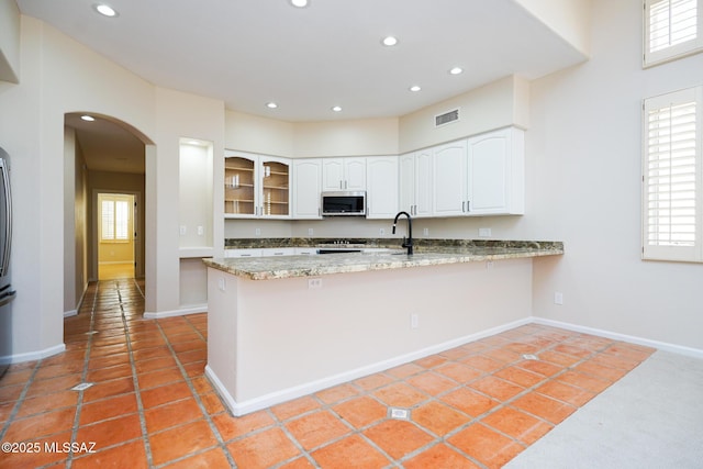 kitchen featuring arched walkways, stainless steel microwave, visible vents, glass insert cabinets, and white cabinets