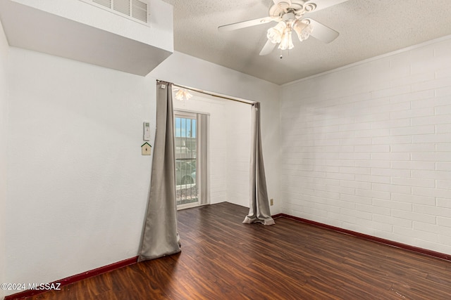 unfurnished room featuring dark wood-type flooring, a textured ceiling, ceiling fan, and brick wall