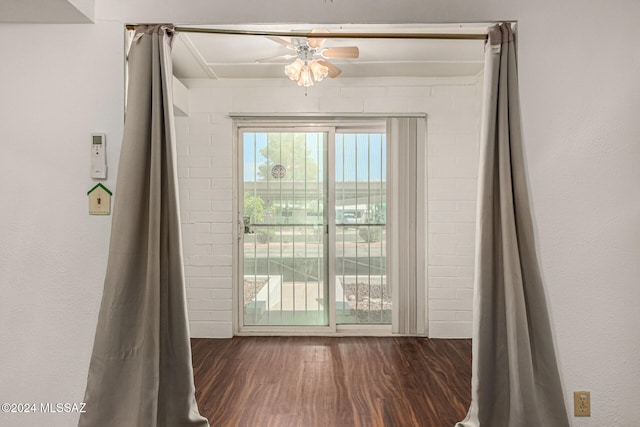 entryway featuring dark wood-type flooring, ceiling fan, and brick wall