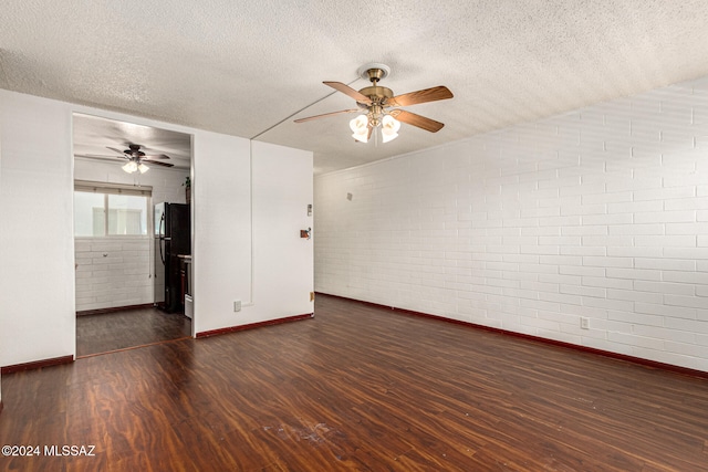 empty room featuring dark wood-type flooring, a textured ceiling, ceiling fan, and brick wall