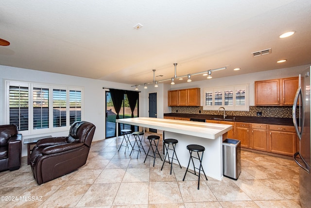 kitchen with decorative backsplash, a kitchen breakfast bar, a kitchen island, sink, and stainless steel refrigerator