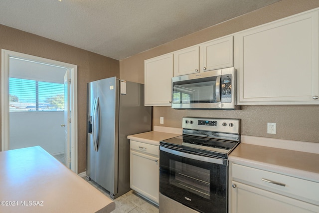 kitchen with white cabinets, light tile patterned floors, a textured ceiling, and stainless steel appliances