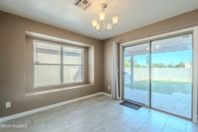 empty room featuring a healthy amount of sunlight, light tile patterned floors, and an inviting chandelier