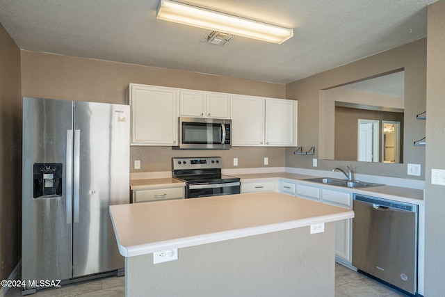 kitchen featuring appliances with stainless steel finishes, a textured ceiling, sink, white cabinets, and a kitchen island