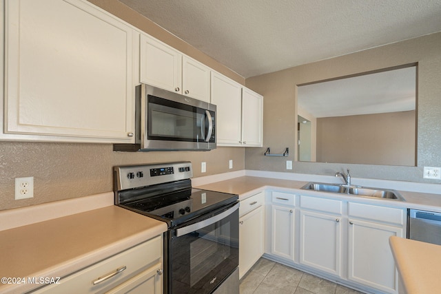 kitchen featuring a textured ceiling, stainless steel appliances, sink, light tile patterned floors, and white cabinetry