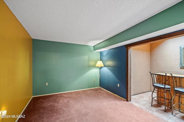 carpeted spare room featuring a textured ceiling and indoor bar