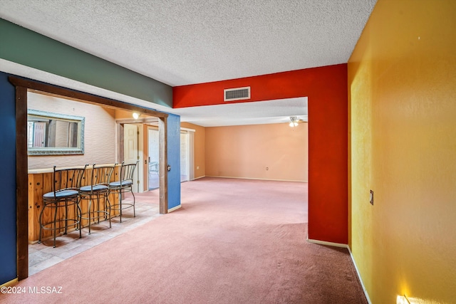 carpeted empty room featuring a textured ceiling, ceiling fan, and indoor bar