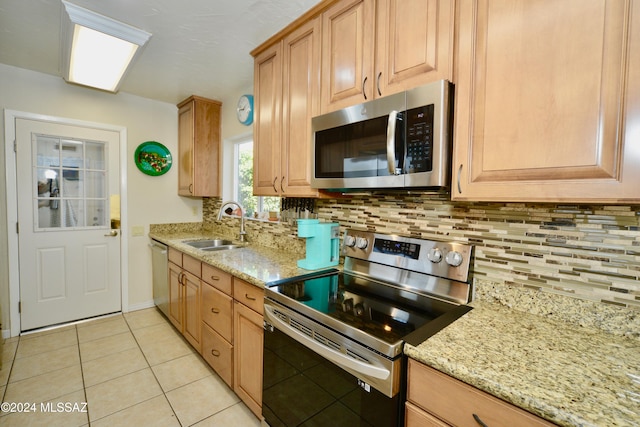 kitchen with stainless steel appliances, sink, light stone counters, light tile patterned floors, and backsplash