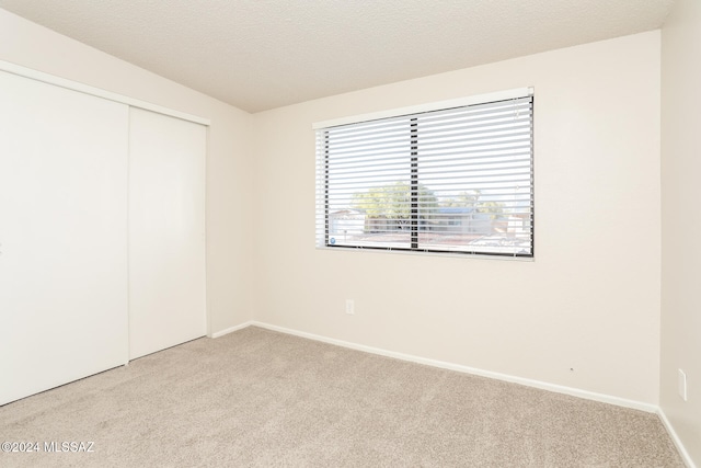 unfurnished bedroom with light carpet, a textured ceiling, and a closet