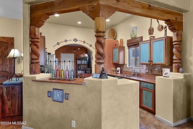 kitchen featuring sink, light tile patterned floors, beamed ceiling, kitchen peninsula, and stainless steel refrigerator