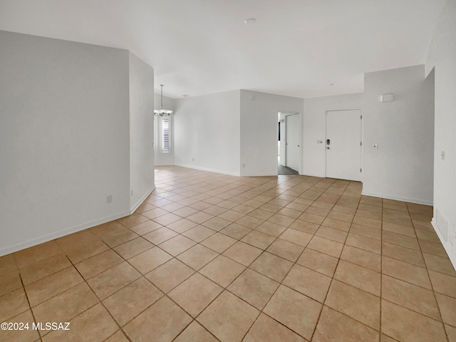 empty room with light tile patterned flooring and a chandelier