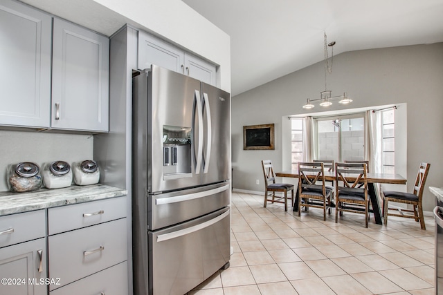 kitchen featuring light stone countertops, stainless steel fridge, pendant lighting, vaulted ceiling, and light tile patterned floors