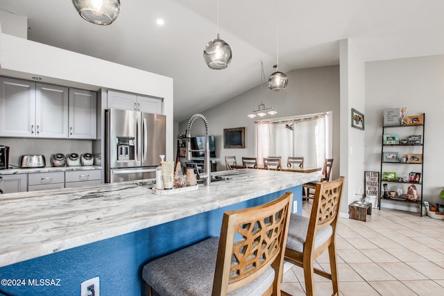 kitchen with hanging light fixtures, stainless steel fridge, vaulted ceiling, gray cabinets, and light tile patterned flooring