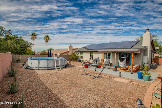 rear view of property featuring a fenced in pool, a patio, and solar panels