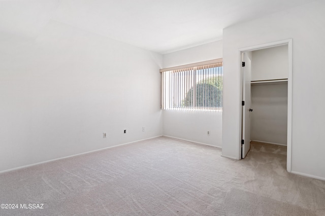 unfurnished bedroom with a walk in closet, light carpet, and a closet