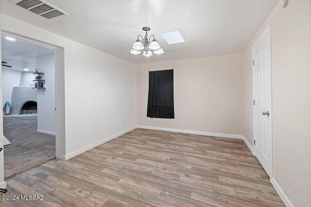 spare room with a notable chandelier, a large fireplace, light wood-type flooring, and a skylight