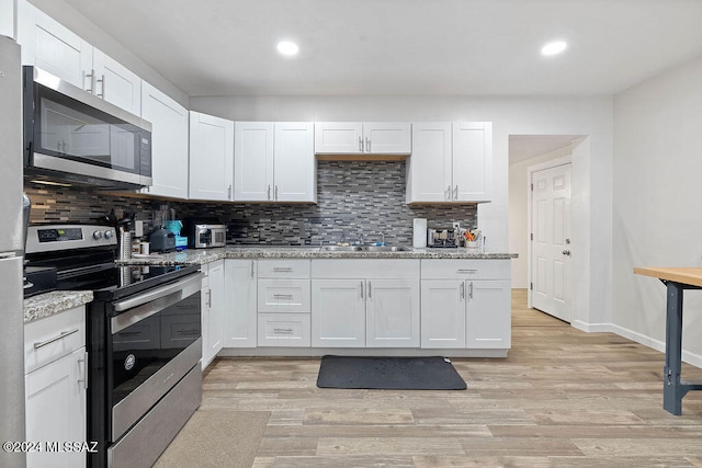 kitchen with light stone countertops, white cabinets, light hardwood / wood-style floors, and appliances with stainless steel finishes